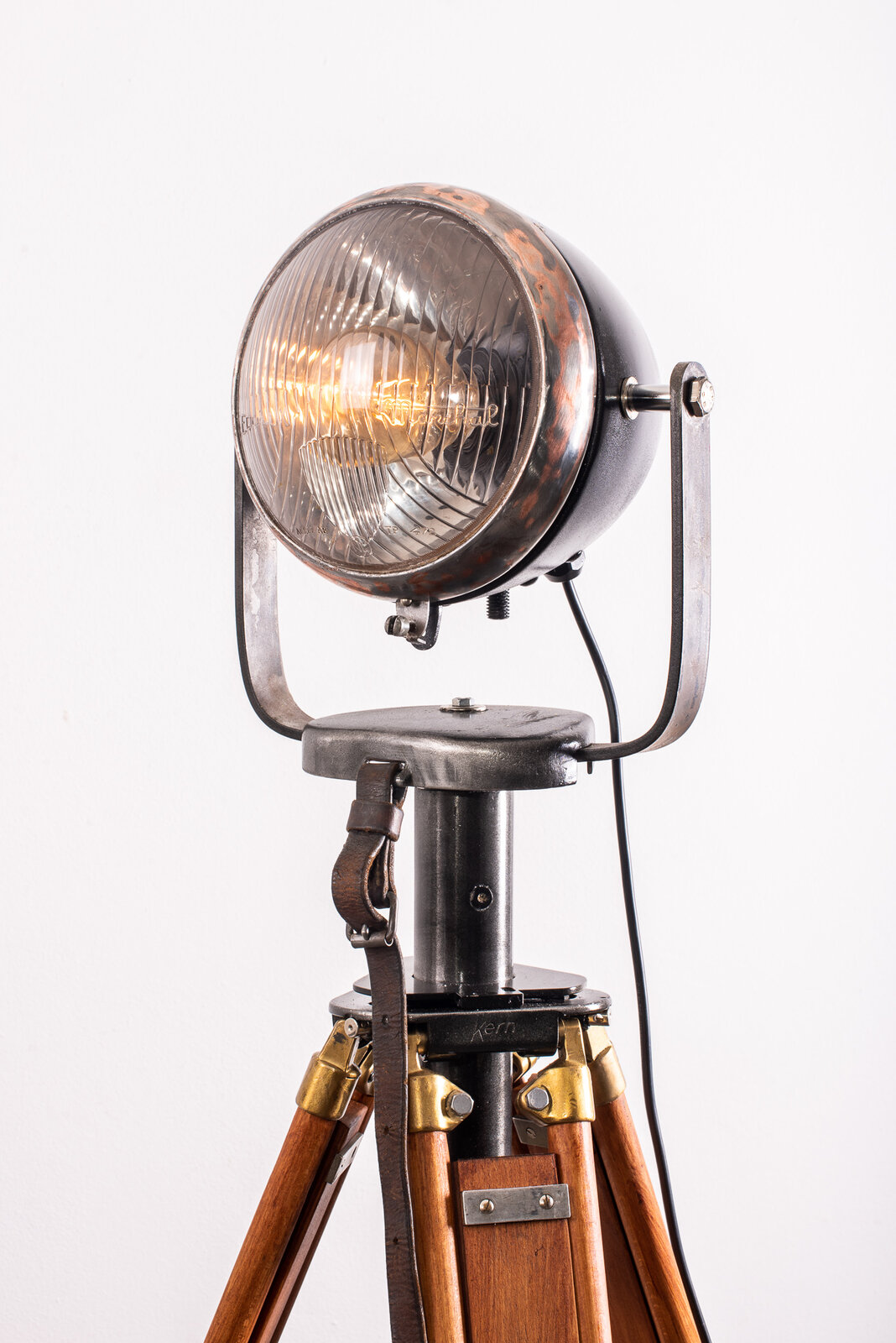 Partie haute du luminaire, phare allumé incliné vers la gauche au-dessus de la tête de trépied Kern