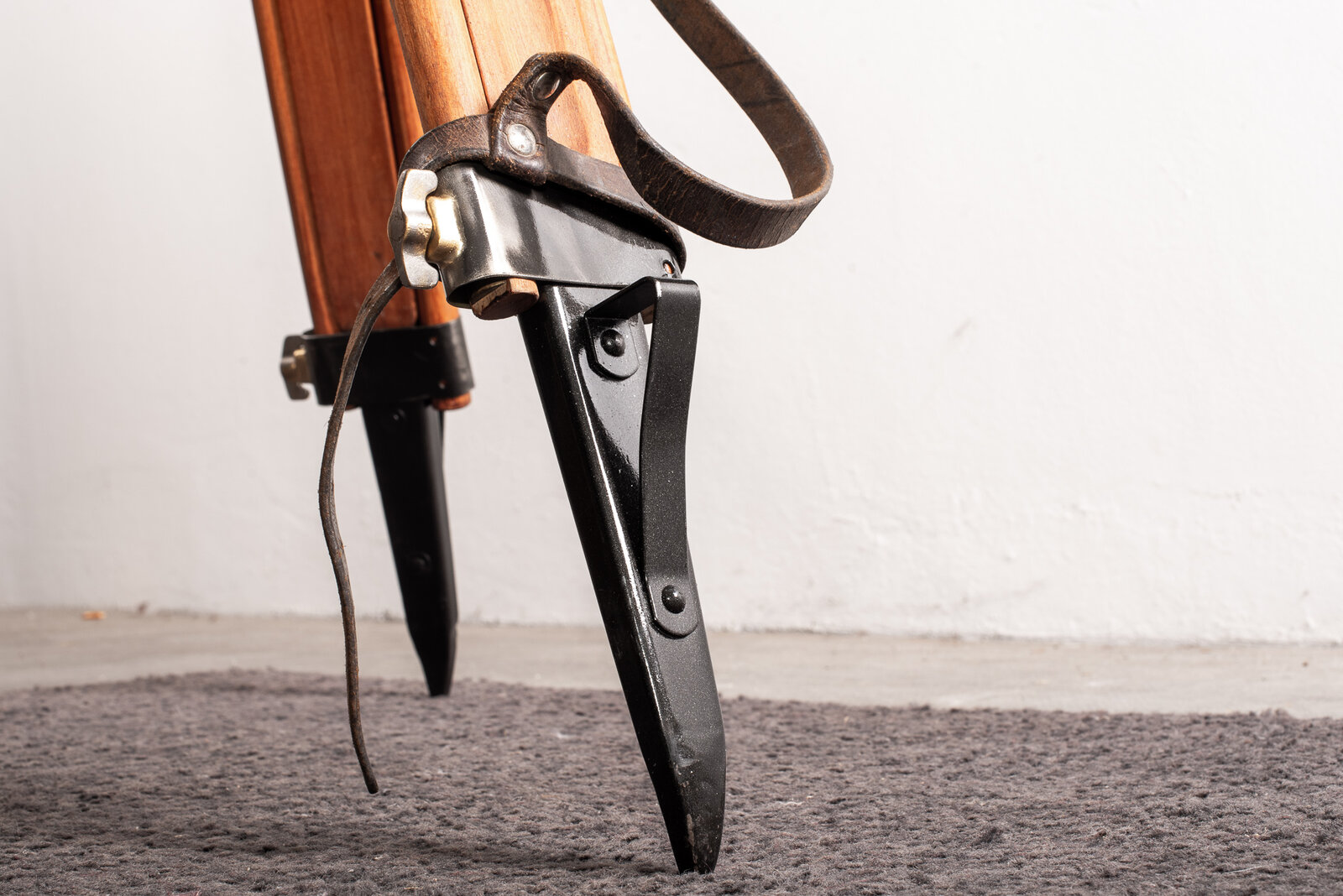 Détail d'un pied de trépied : pointe en acier noir, sangle de cuir et collier laiton