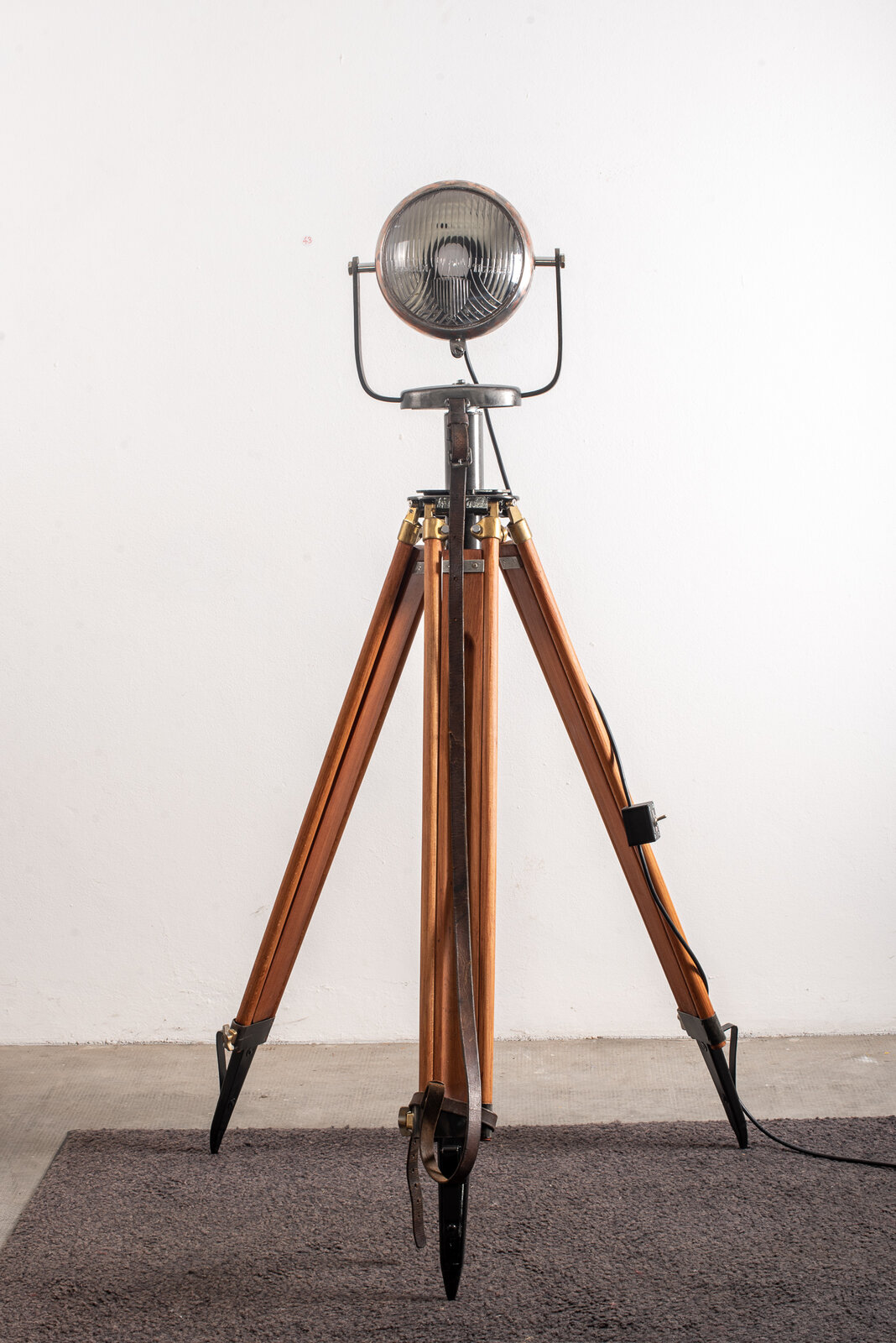 Luminaire vu de face, optique dirigée vers l'objectif, trois jambes de bois déployées sur le sol